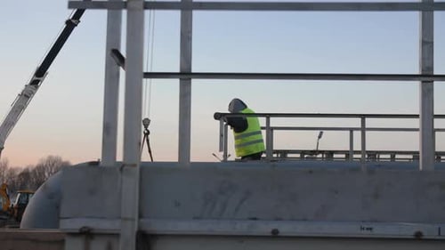Worker in Yellow Vest Leans on Ground Railing Over Pipelines