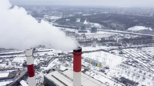 Aerial Observation of Snowy Industrial City with Two Huge Smoking Factory Pipes at the Foreground.