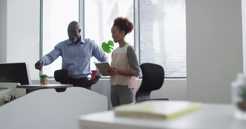 Diverse businessman and businesswoman talking, woman using digital tablet in office
