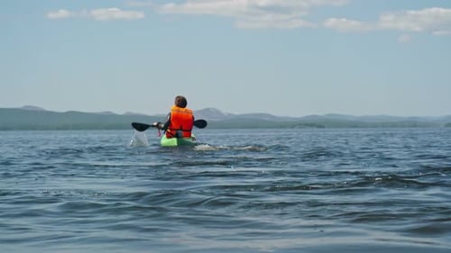 Kayaker Paddles on Lake Wearing Orange Life Jacket