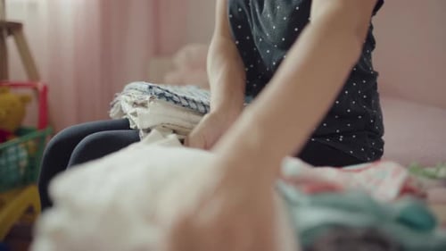 Adult Folding Baby Clothes in Bedroom at Home