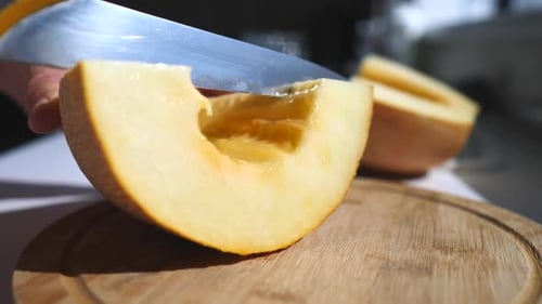 Nahaufnahme Frauenhände schneiden frische Melone mit Messer auf Holzschneidebrett