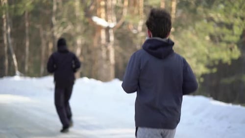 Adults Jogging on a Snowy Path in Winter