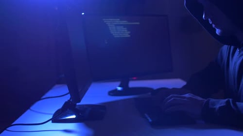 Hooded Figure Typing in Dark Blue Room