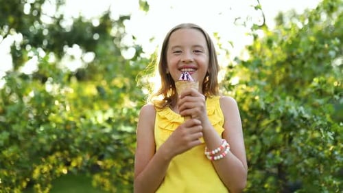 Happy girl eating italian ice cream cone smiling while resting in park on summer day