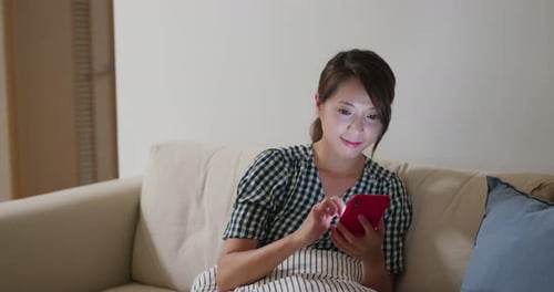 Woman Using Smartphone on Couch Indoors at Night