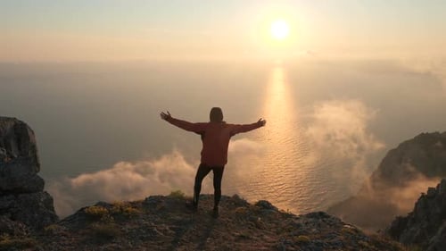 Silhuette of Young Man Arms Outstretched Observing Beautiful Dramatic Colorful Sunset Above a Sea