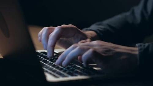 Hände eines Mannes, der nachts am Laptop arbeitet.