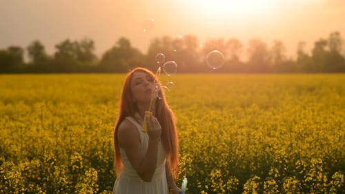Young Redhair Woman Blowing Bubbles at the Camera Outdoors in Summer Meadow