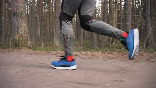 Man in Sneakers Runs on Forest Path Strewn with Pine Cones