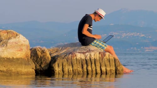 Un tipo independiente que trabaja cerca de las rocas y el mar. Hombre de negocios de vacaciones en un desierto tropical