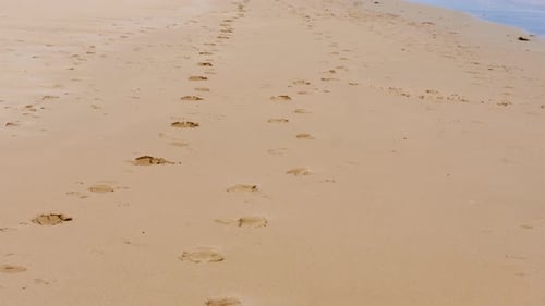 Footprints in the sand at a beach panning up to an ocean horizon with waves crashing the shore.