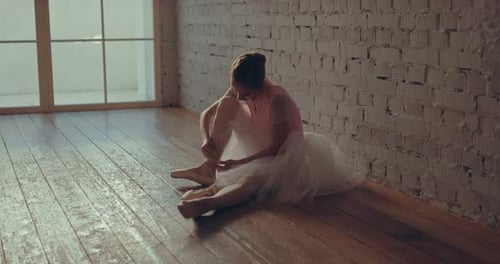 Ballerina Tying Ballet Shoes on Wooden Floor