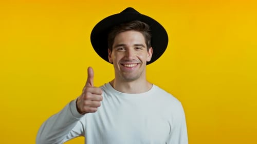 Smiling Man in Hat Gives Thumbs Up on Yellow