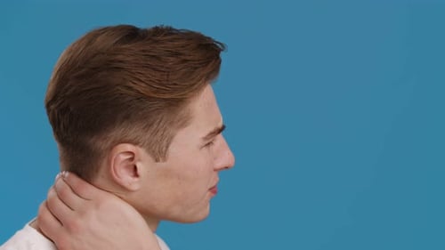 Young Man Suffering From Neck of Pain Massaging It Profile Portrait Blue Studio Background