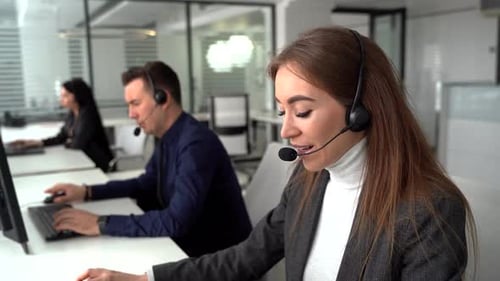 eine schöne junge Geschäftsfrau und ein schöner Geschäftsmann in Headsets, die während der Arbeit Laptops benutzen