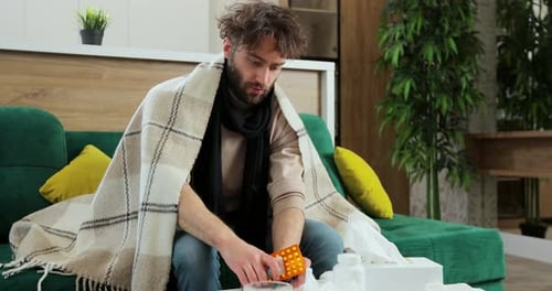 Ill Man Examining Pills on Couch Indoors
