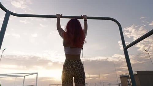 Athletic Woman Pulls Up on Horizontal Bar on Background of a Beautiful Sunset