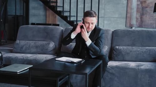 Handsome Man European Appearance in Classic Clothes in a White Shirt Sits in a Stylish Dark Office