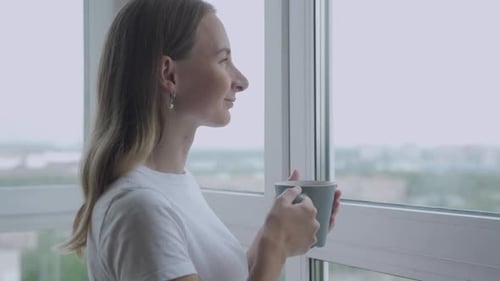 Woman Drinking from Mug and Gazing out Window
