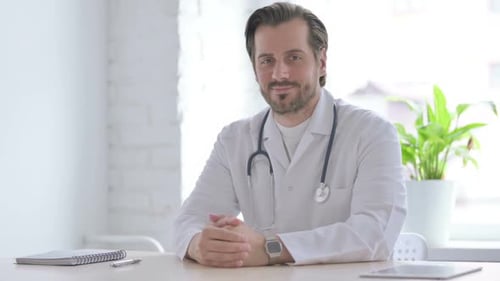 Young Doctor Smiling at Camera While Sitting in Clinic