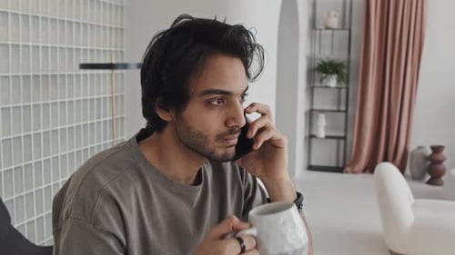 Man Talking on Phone and Drinking Tea Indoors