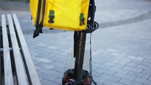 Foto de pedestal de un patinete eléctrico en la calle de la ciudad con mochila amarilla de entrega de comida colgada