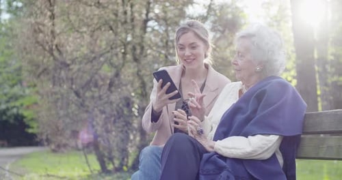 Woman and Senior Grandmother Using Smartphone Device at Park