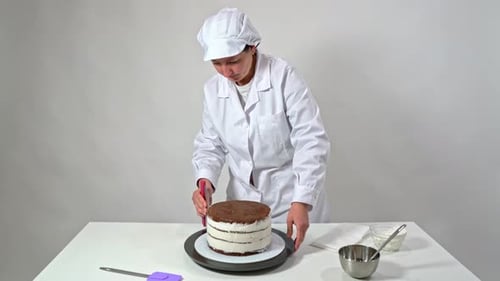 Baker Removes the Excess Cream From the Sides of a Chocolate Cake By Rotating the Stand and Using a