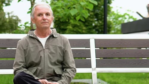 Stylish Elderly Man with Long Hair Smiling on Bench in Public City Park
