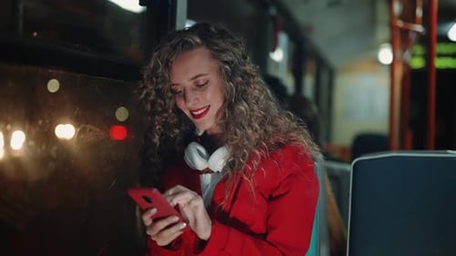 A Smiling Curly Woman is Using Smartphone and Reading Messages in Bus