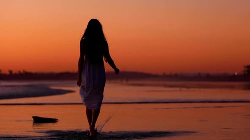 Asiatin genießt bei Sonnenuntergang einen Strandspaziergang. Zeitlupe.