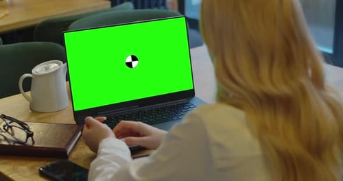 Mockup View of Woman Using Laptop with Blank Green Screen in Modern Loft Cafe