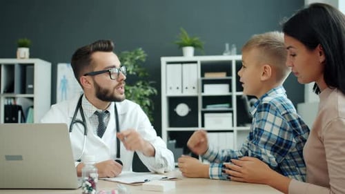 Child Talking To Friendly Children's Doctor in Hospital While Mother Laughing