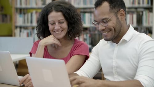 Cheerful Colleagues Sitting at Library and Communicating