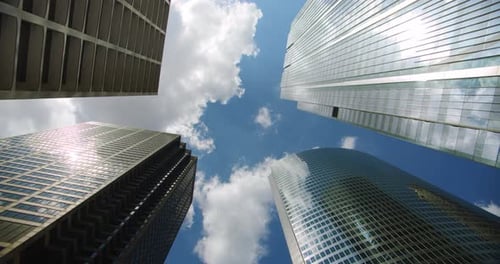 Mirando hacia arriba en edificios de rascacielos de negocios en el centro, nubes rodando en el cielo y reflexiones sobre