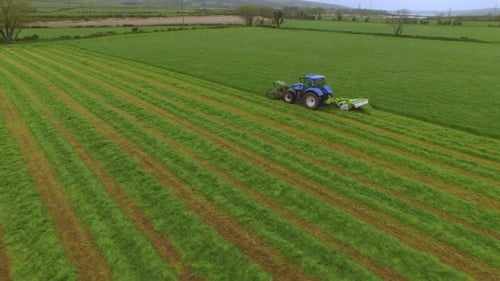 Vue aérienne d'un tracteur coupant l'herbe dans un grand champ vert.