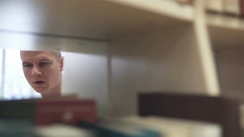 Man Browsing Colorful Bookshelf in a Library