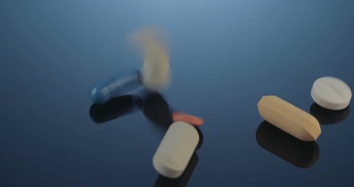 Colorful Pills and Capsules Falling onto Reflective Surface