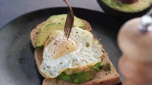 Fork Piercing Yolk of Egg on Avocado Toast