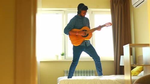 Man Playing Guitar on Bed in Sunny Bedroom