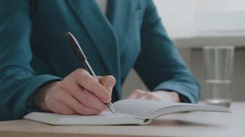 Close Up Female Hands Caucasian Woman in Green Jacket Sitting at Desk Holding Pen Making Notes in
