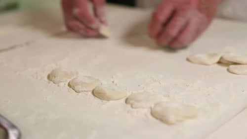 Chef flattens a ball of dough using his palms on a floured countertop.