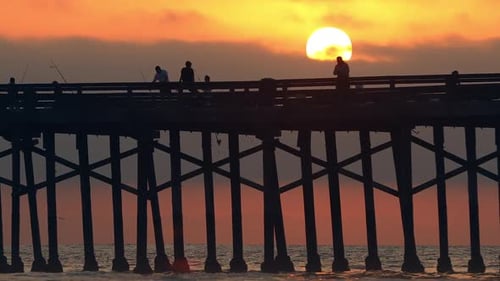 People fishing on top of pier against the sun in the sky