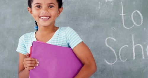 Smiling Schoolgirl Holding Books in Front of Chalkboard