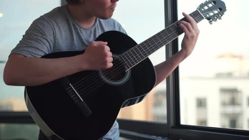 Close up of lonely man playing guitar against an opened window