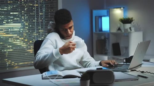 Homme métisse travaillant sur ordinateur parlant par smartphone et buvant une tasse de thé