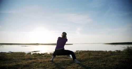 Silhouette of Young Sporty Woman Engaged in Gymnastics on Background Sky and Lake. V4