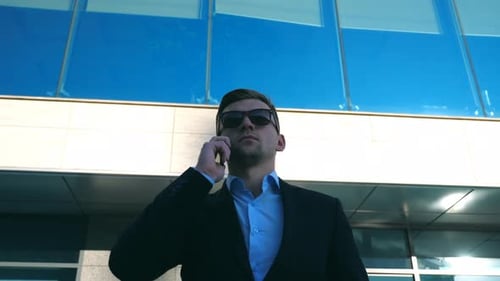 Portrait of Young Businessman in Sunglasses Talking on Phone Outdoor Near Office