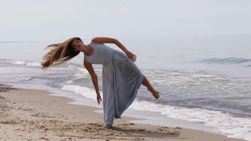 Nice Young Woman in a Long Dress Dancing on The Beach